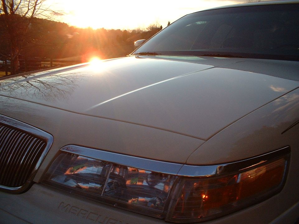 Gold Mercury sedan front with sun flare over the hood at sunset