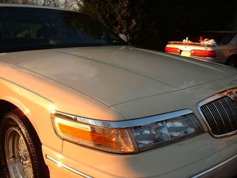 1996 Mercury Grand Marquis - Front corner of a beige 1996 Mercury Grand Marquis, showing the grille and headlights, with another car visible in the background.