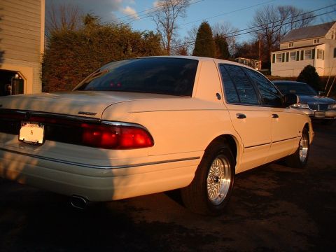 1996 Mercury Grand Marquis - A cream-colored sedan is parked outside a house, with another car visible in the background.