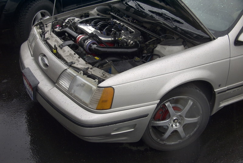 Silver 1990 Ford Taurus front quarter view with hood open, showing engine and red brake calipers
