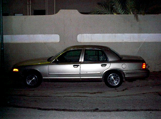 Gold Crown Victoria sedan parked at night against a concrete wall