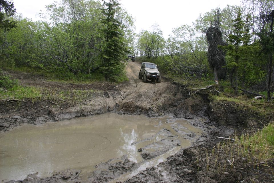 Two SUVs driving up a muddy hill, one in foreground, one further up
