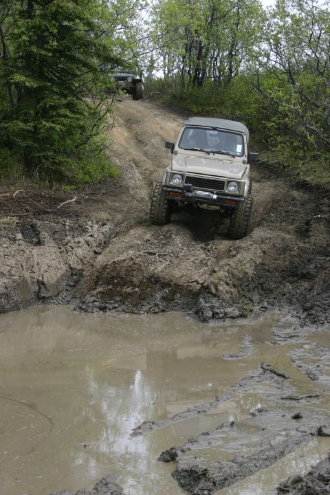 2003 Jeep TJ - Two off-road vehicles tackle a challenging muddy trail with trees on either side.