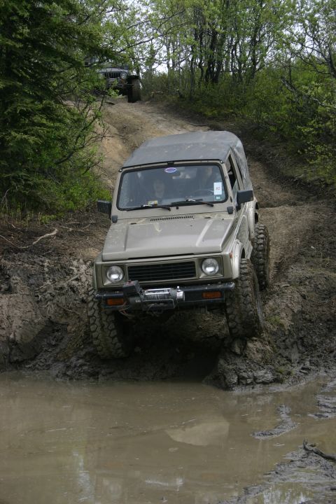 2003 Jeep TJ - Two off-road vehicles navigate a challenging muddy trail with deep puddles and steep inclines.