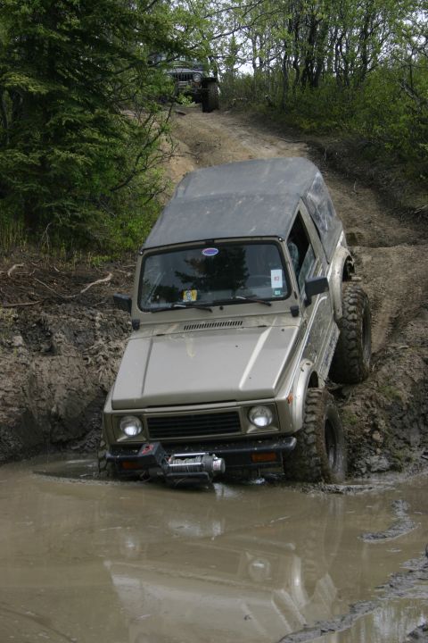 2003 Jeep TJ - A Suzuki Samurai navigates a muddy trail, with another off-road vehicle in the background.
