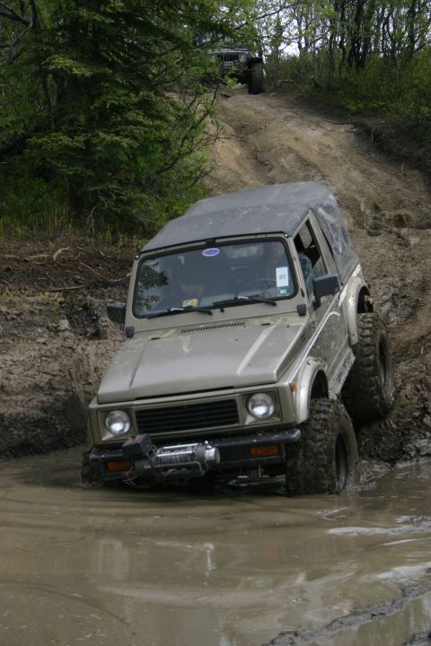2003 Jeep TJ - This off-road vehicle tackles a challenging muddy incline during an outdoor meet and greet event.
