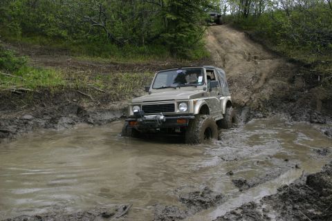 2003 Jeep TJ - A Suzuki Samurai navigates a muddy trail with another vehicle visible in the background.