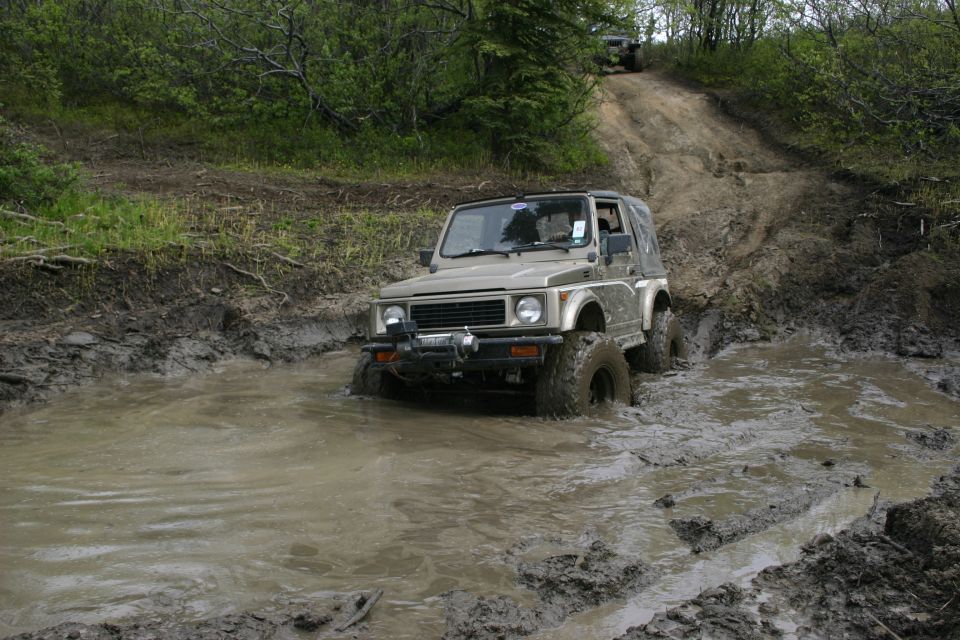 Tan Suzuki Samurai driving through a mud puddle on a dirt track