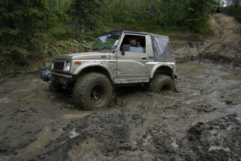 2003 Jeep TJ - Suzuki Samurai navigating a challenging muddy trail during an off-road event.