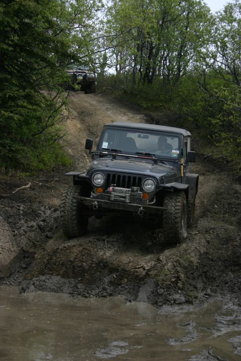 2003 Jeep TJ - A 2003 Jeep Wrangler tackles a challenging muddy off-road course with another vehicle visible in the background.