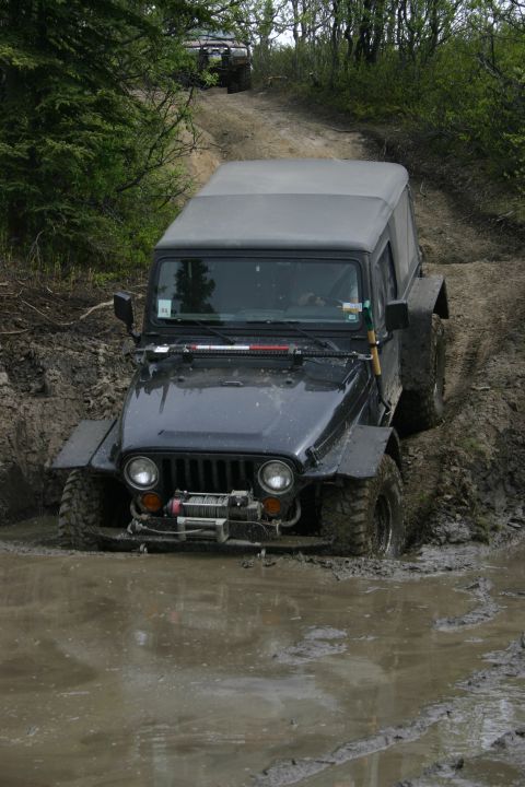 2003 Jeep TJ - A black Jeep Wrangler TJ navigates a muddy trail, with another vehicle visible in the background.