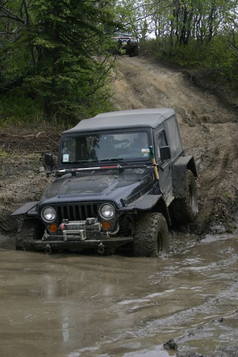 2003 Jeep TJ - A 2003 Jeep TJ tackles a challenging muddy off-road course, with another Jeep visible in the background.