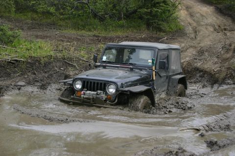 2003 Jeep TJ - A black 2003 Jeep TJ navigates a muddy trail, with its front tires submerged in water and mud.