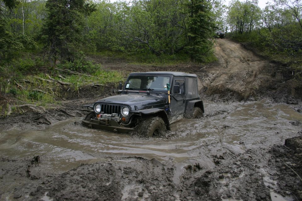 Black 2003 Jeep TJ stuck in deep mud on an off-road trail