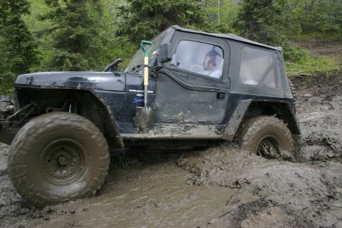 2003 Jeep TJ - A black Jeep Wrangler TJ navigates a muddy trail, with a shovel mounted on the driver's side door.