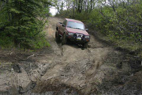 2003 Jeep TJ - A red 2003 Toyota Tacoma navigates a challenging muddy incline during an off-road event.