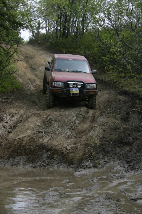 2003 Jeep TJ - Pickup truck descends a challenging muddy trail with trees on either side.