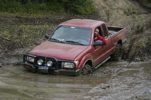 2003 Jeep TJ - A red pickup truck is stuck in a muddy puddle, with the driver looking out the window.