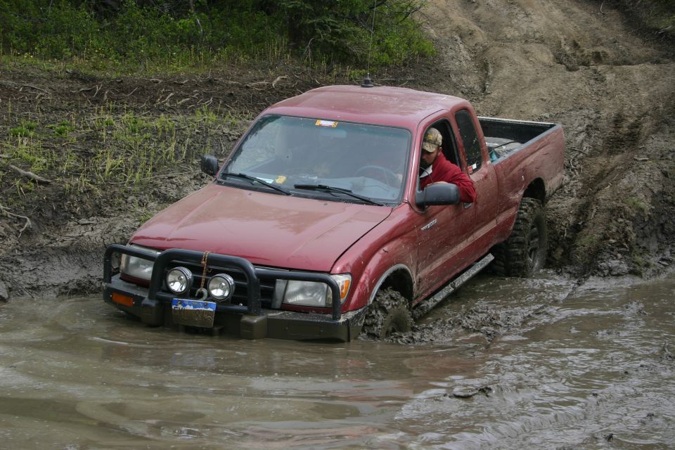 Red pickup truck stuck in deep mud, driver visible inside