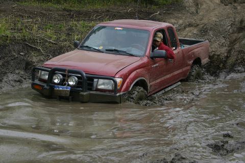 2003 Jeep TJ - A red pickup truck is stuck in a muddy puddle, with its tires submerged.