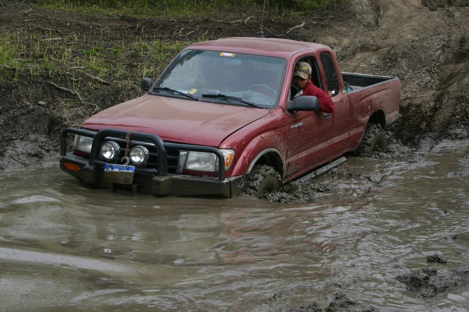 Red pickup truck with a brush guard and auxiliary lights stuck in deep mud