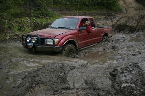 2003 Jeep TJ - This red Toyota Tacoma is stuck in the mud while navigating an off-road trail.