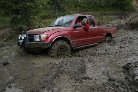 2003 Jeep TJ - A driver navigates a challenging muddy terrain, with the front of the truck submerged in thick mud.