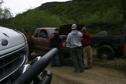 2003 Jeep TJ - People inspect the engine of a red pickup truck during an off-road event.