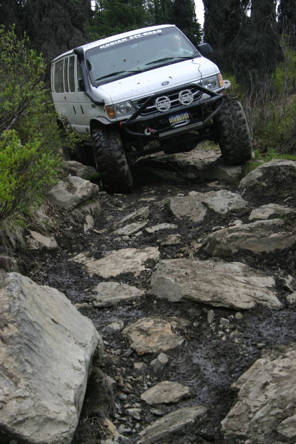 White Ford van with snorkel and big tires navigating a rocky trail
