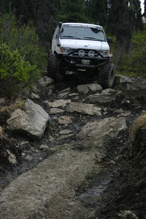 2003 Jeep TJ - A modified white van tackles a challenging, rocky off-road path.