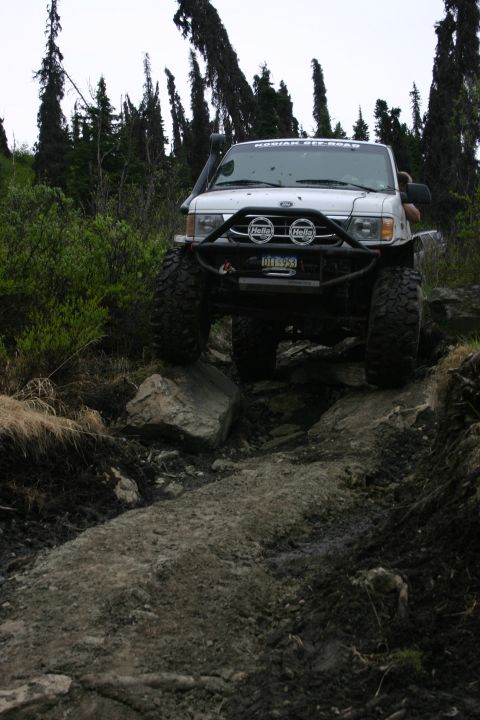 2003 Jeep TJ - A modified white SUV tackles a challenging rocky trail in a wooded area.