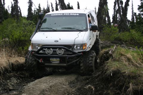 2003 Jeep TJ - A white van navigates a muddy off-road trail surrounded by trees.