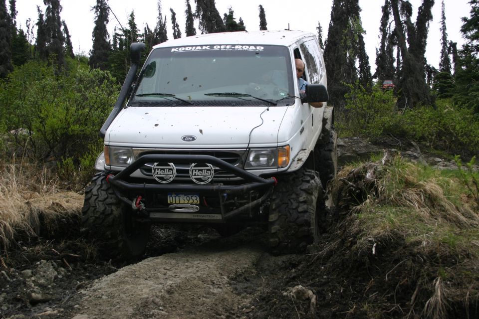 White van with off-road tires and snorkel on a dirt path, front view