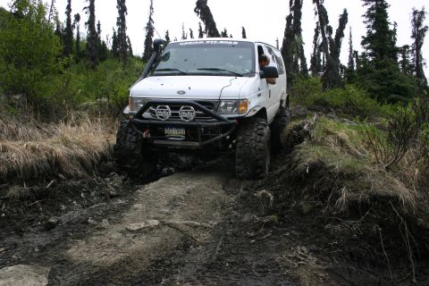2003 Jeep TJ - A white van equipped for off-roading navigates a challenging muddy and rocky terrain.