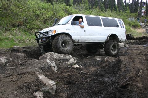 2003 Jeep TJ - A man drives a modified van through a challenging off-road course with trees in the background.