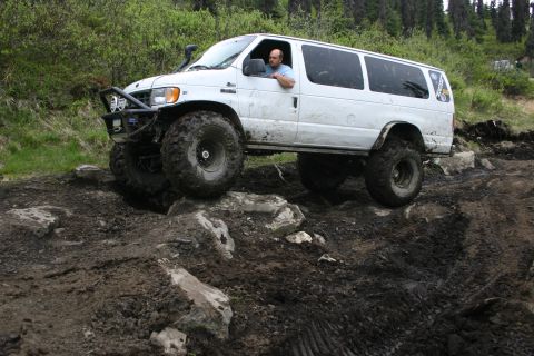 2003 Jeep TJ - A modified white van navigates a challenging muddy and rocky off-road course.