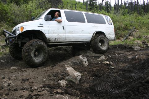 2003 Jeep TJ - A white van modified for off-road use tackles a challenging muddy terrain.