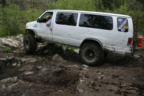 2003 Jeep TJ - Modified white van tackling rough off-road terrain with large tires.
