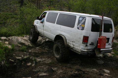 2003 Jeep TJ - This modified van is navigating a challenging off-road trail, equipped with a jerry can and shovel on the rear.