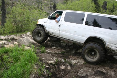 2003 Jeep TJ - A white van with oversized tires is driven over a challenging rocky terrain.