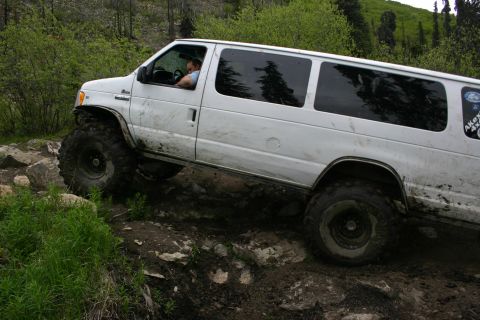 2003 Jeep TJ - A white van with large off-road tires is shown traversing a challenging rocky path.