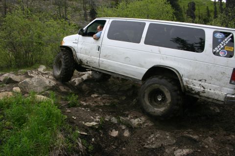 2003 Jeep TJ - White van with off-road tires navigating a muddy, rocky path.