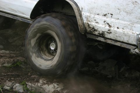 2003 Jeep TJ - A white off-road vehicle navigates challenging terrain, its tire kicking up dirt.