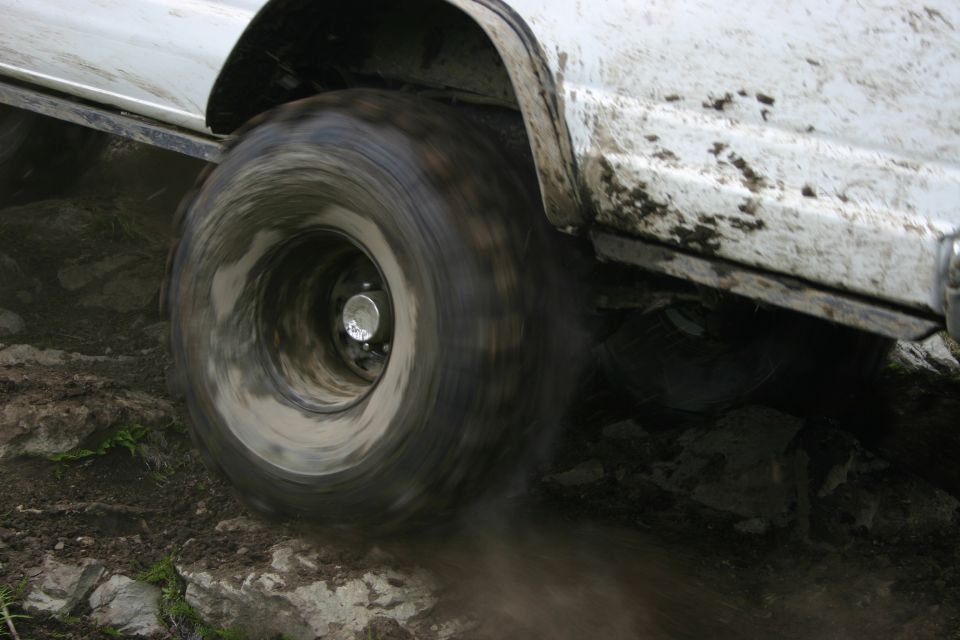 White off-road vehicle tire spinning on rocky, muddy terrain