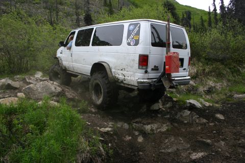 2003 Jeep TJ - A white van navigates a challenging rocky terrain, equipped with oversized tires and a mounted jerry can for extended journeys.