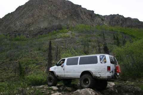 2003 Jeep TJ - A modified van navigates a challenging rocky path in a mountainous, wooded area.