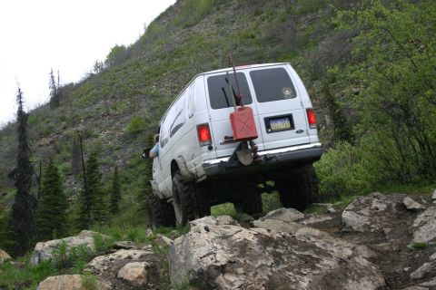 2003 Jeep TJ - A white van navigates a challenging rocky terrain on an incline, equipped with off-road gear.