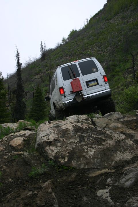 2003 Jeep TJ - A white van navigates a challenging rocky trail, equipped with a red jerrycan and shovel for off-road excursions.