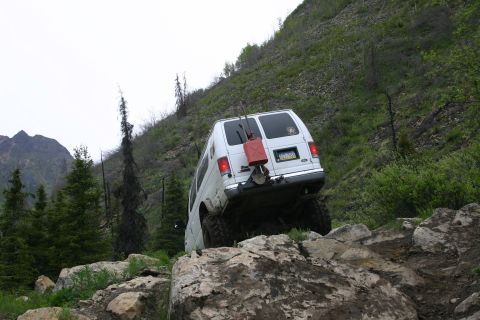 2003 Jeep TJ - A white van navigates a challenging rocky path on a steep, vegetated mountainside.