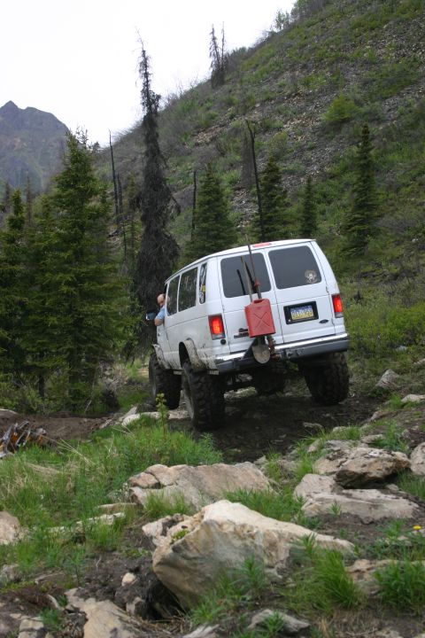 2003 Jeep TJ - A white van navigates a challenging, rocky trail in a mountainous, wooded area.